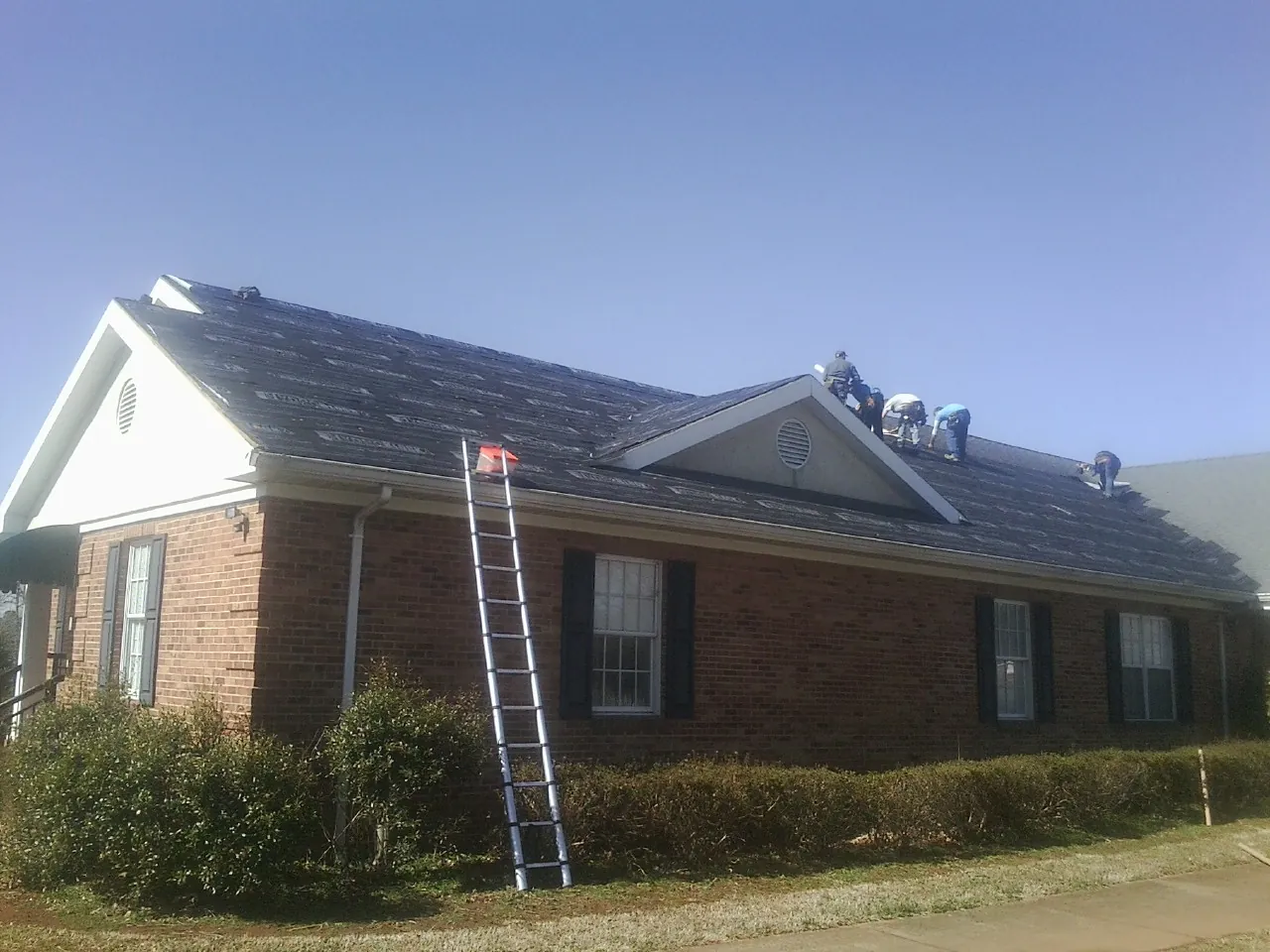 Crew tearing shingles off a brick ranch roof with a ladder set — Emergency Roof Repair work by our crew in Linden