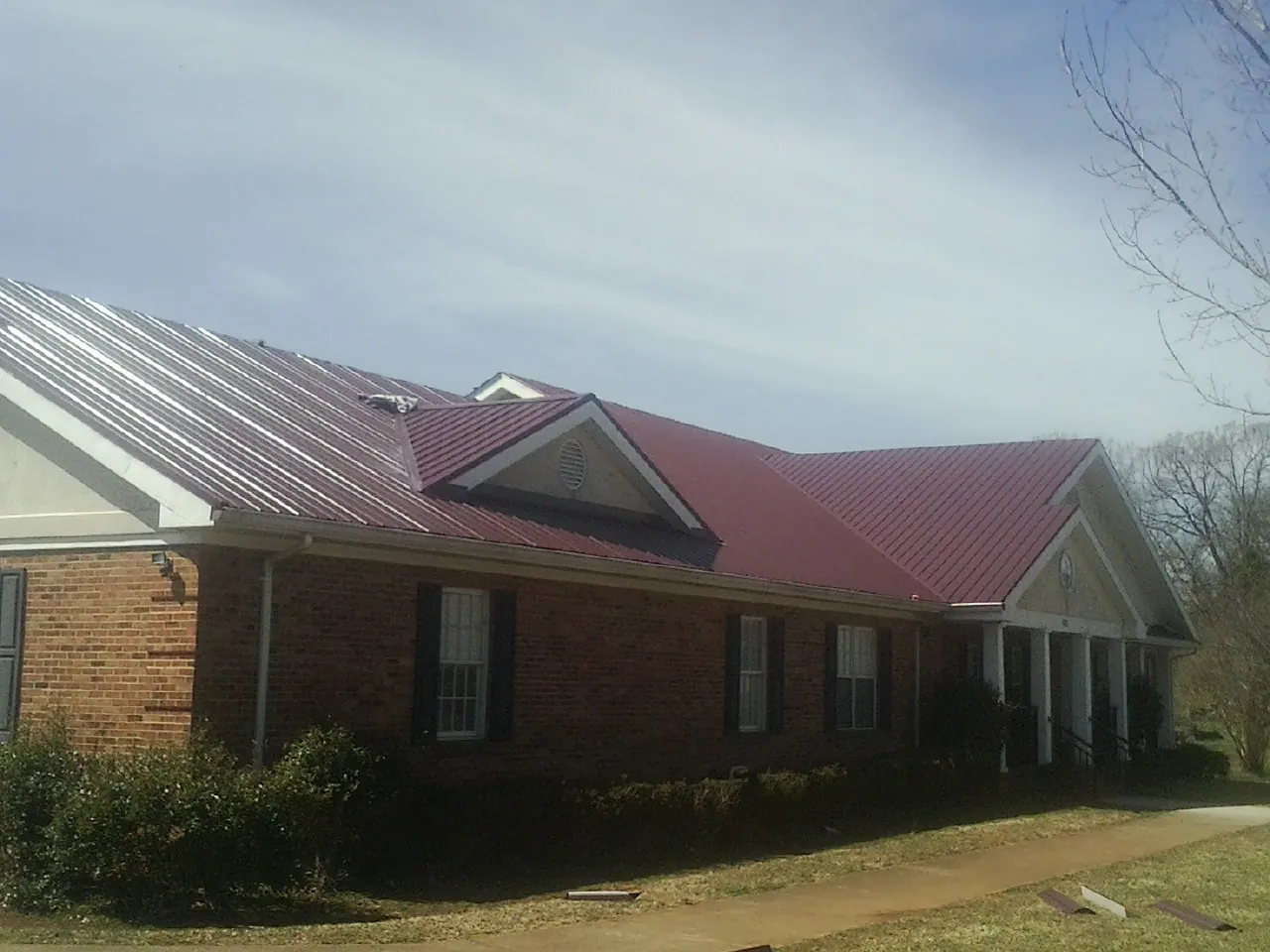 Red metal roof with gabled entries on a long brick building, from a Hail Damage Roof Repair job in Linden